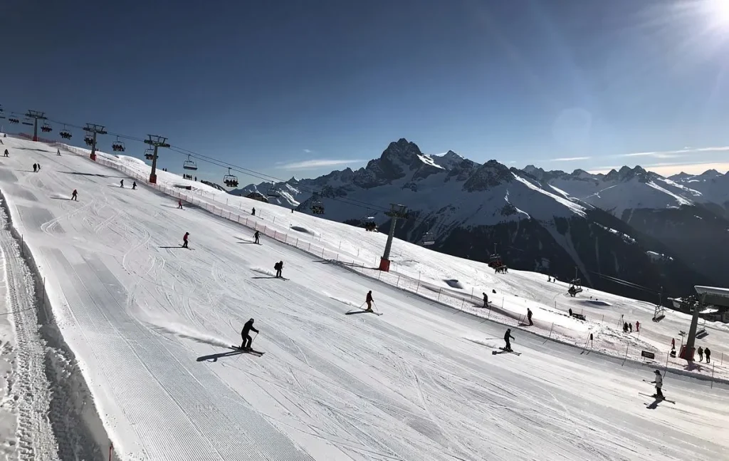 Vue d'une webcam montrant des skieurs sur les pistes enneigées de Saint-Lary sous un ciel bleu et ensoleillé.